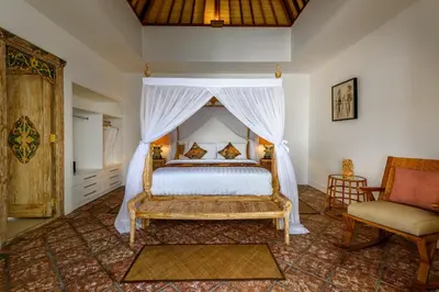 a bedroom with a canopy bed and a chair at Hevea Villas in Seminyak