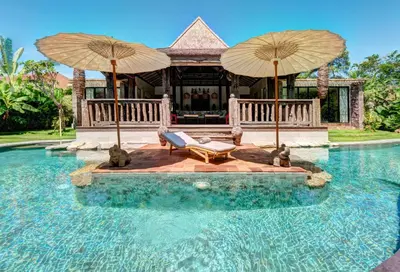 a house with two umbrellas and a swimming pool at Villa River Garden Canggu in Kerobokan