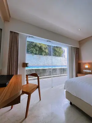 a bedroom with a bed and a desk and a window at The Capital Hotel and Resort Seminyak in Seminyak