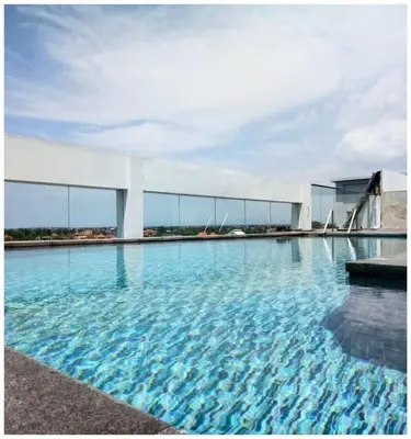 a swimming pool with blue water in front of a building at The Capital Hotel and Resort Seminyak in Seminyak