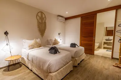 two beds in a hotel room with a bathroom at Villa Hana by Alfred in Bali in Seminyak