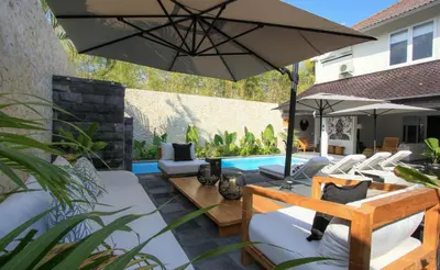 a patio with an umbrella and chairs and a pool at Mahasari Villa in Seminyak