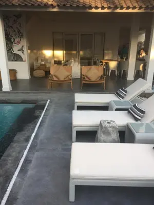a pool with white benches and chairs next to a building at Mahasari Villa in Seminyak