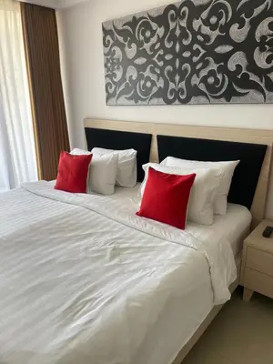a white bed with two red pillows on it at Stylish 2 Bedroom Penthouse Apt, Newly Refreshed, 50 Mbps, Pool, Gym, Resto in Kuta