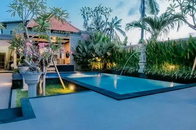 a swimming pool in front of a house with palm trees at The Lavana Arimanu Kuta in Kuta
