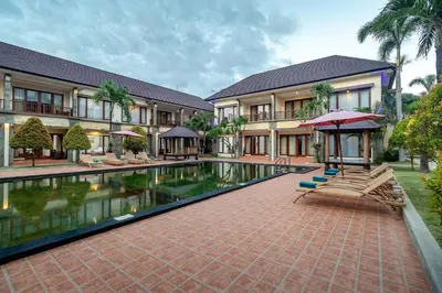 a resort with a swimming pool with two chairs and an umbrella at Vidi Boutique Hotel in Nusa Dua