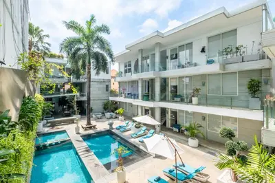 an apartment building with a pool and palm trees at AQ-VA Hotel & Villas Seminyak in Legian