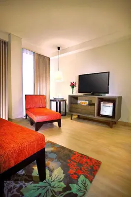 a living room with a flat screen tv and a red chair at Harper Kuta Hotel by ASTON in Legian