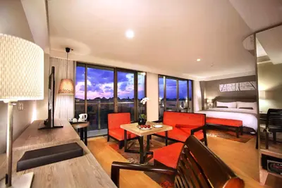 a hotel room with a bed and a living room with a table at Harper Kuta Hotel by ASTON in Legian
