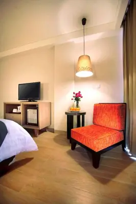 a bedroom with a red chair and a tv at Harper Kuta Hotel by ASTON in Legian