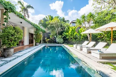 a pool with chairs and umbrellas next to a house at Central Seminyak Villa Martini in Seminyak