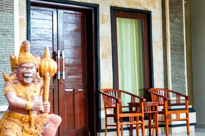 a statue standing in front of a building with two chairs at Putu Guest House 2 in Canggu