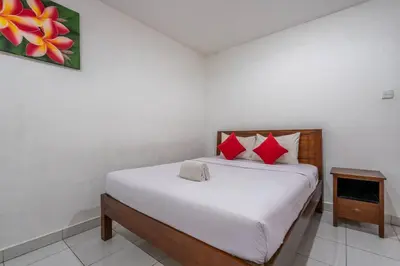 a bedroom with a bed with white sheets and red pillows at Ganandra Stay Denpasar in Denpasar