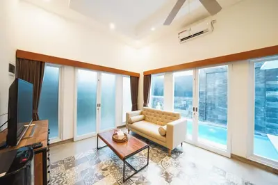 a living room with a couch and a tv and windows at Umaja Villa in Seminyak