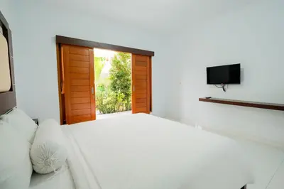 a bedroom with a white bed and a television at Kadek Bagus Guesthouse Denpasar Mitra RedDoorz in Kerobokan