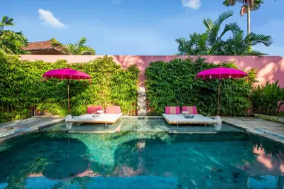 a swimming pool with two pink chairs and umbrellas at PinkPrivate Sanur - for Cool Adults Only in Sanur