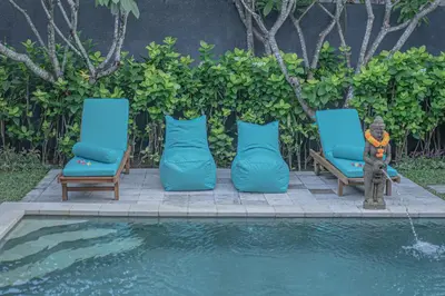 two blue chairs and a statue next to a pool at Leluhur 1 Private Pool Villa in Seminyak
