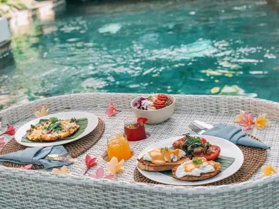 a table topped with plates of food next to a pool at Beyond Bespoke Villas in Seminyak