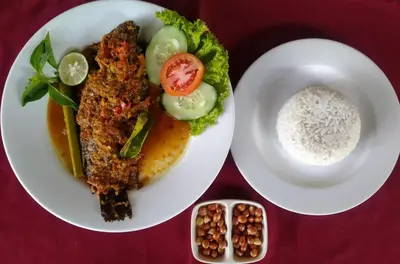 a plate of food with rice and meat and vegetables at Ganga Hotel & Apartment in Denpasar