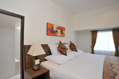 a bedroom with a large white bed and a lamp at Ganga Hotel & Apartment in Denpasar