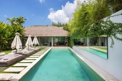 a swimming pool with chairs and umbrellas next to a house at Saga Villas ULTRA in Seminyak
