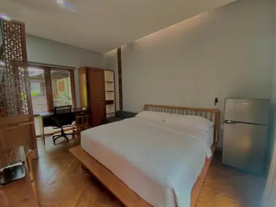 a bedroom with a white bed and a refrigerator at Ruang Tekuni in Legian