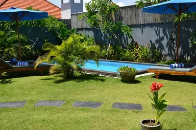 a swimming pool in a yard with benches and umbrellas at Villa Eden Seminyak in Seminyak