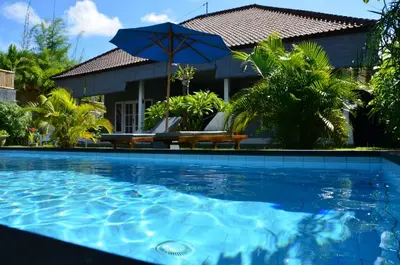 a swimming pool with an umbrella and a house at Villa Eden Seminyak in Seminyak