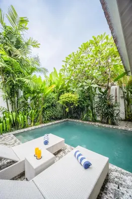 a swimming pool with white chairs and a swimming pool at Villa Jolaine in Seminyak