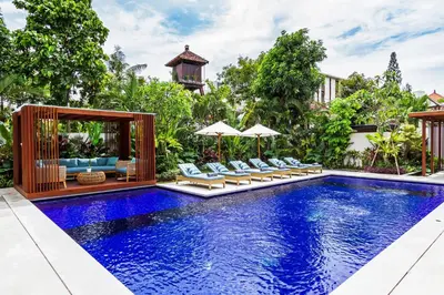 a pool with chairs and umbrellas next to a house at THE BOTANICAL 6 BED LUXURY 900 meter from beach in Seminyak