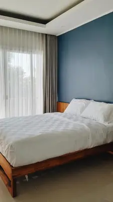 a bedroom with a bed with a blue wall and a window at RakaAyu Kuta in Kuta