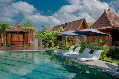 a pool with chairs and umbrellas next to a house at Moson Villa Legian in Legian