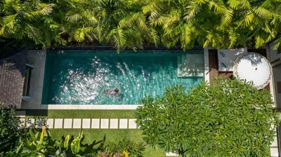 a person swimming in a swimming pool with trees at Villa Songket in Kerobokan