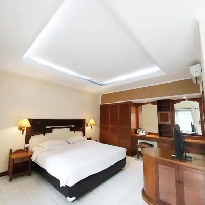 a bedroom with a large white bed and a desk at Bali Bungalo Hotel in Kuta