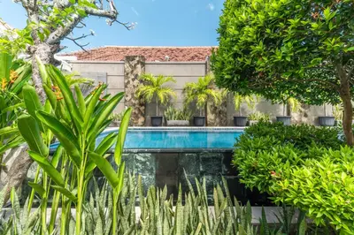 a swimming pool in front of a building with trees at Svarna Suites Seminyak in Seminyak