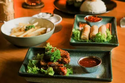 a table with two plates of food and a bowl of fries at Grandmas Plus Hotel Airport in Kuta