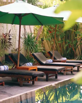 a row of lounge chairs with umbrellas next to a pool at Grandmas Plus Hotel Airport in Kuta