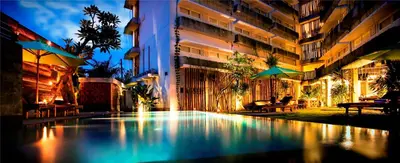 a swimming pool in front of a building at night at Grandmas Plus Hotel Airport in Kuta