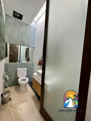 a bathroom with a toilet and a door with a logo at Villa di Sawah - by Unicorn Villas Bali in Kerobokan