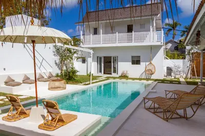 a villa with a swimming pool and two chairs and an umbrella at Villa M2 Seminyak by Alfred in Bali in Seminyak