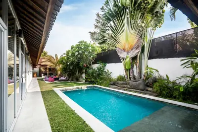 a swimming pool in the backyard of a house with a palm tree at Villa Baik Baik by BaliSuperHost in Seminyak