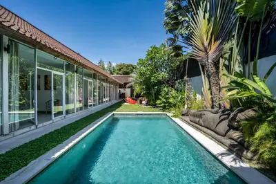 a swimming pool in front of a house with a palm tree at Villa Baik Baik by BaliSuperHost in Seminyak