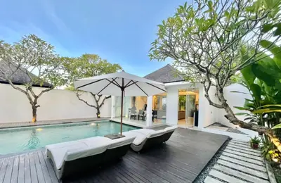 an outdoor swimming pool with an umbrella and two lounge chairs at Alami Luxury Villa in Seminyak