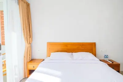 a bedroom with a white bed with a wooden headboard at Dharma Guest House Seminyak RedPartner in Seminyak
