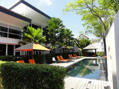 an outdoor swimming pool with orange chairs and an umbrella at Bali Yarra Villas - Seminyak in Seminyak