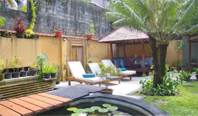 a garden with a pond and chairs and a palm tree at Villa Naga Maya in Legian