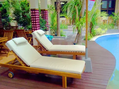 two lounge chairs and an umbrella next to a swimming pool at Manggar Indonesia Hotel in Kuta