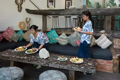 two women are standing near a couch with plates of food at Phinisi Villas - Seminyak Beach in Seminyak