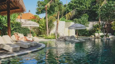 a woman sitting on chairs next to a swimming pool at Amnaya Resort Nusa Dua in Nusa Dua
