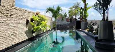 a swimming pool next to a brick wall with palm trees at Villa Mimpi Bali in Jimbaran